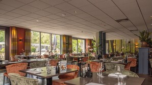 Um restaurante com várias mesas e cadeiras, grandes janelas e plantas dentro.