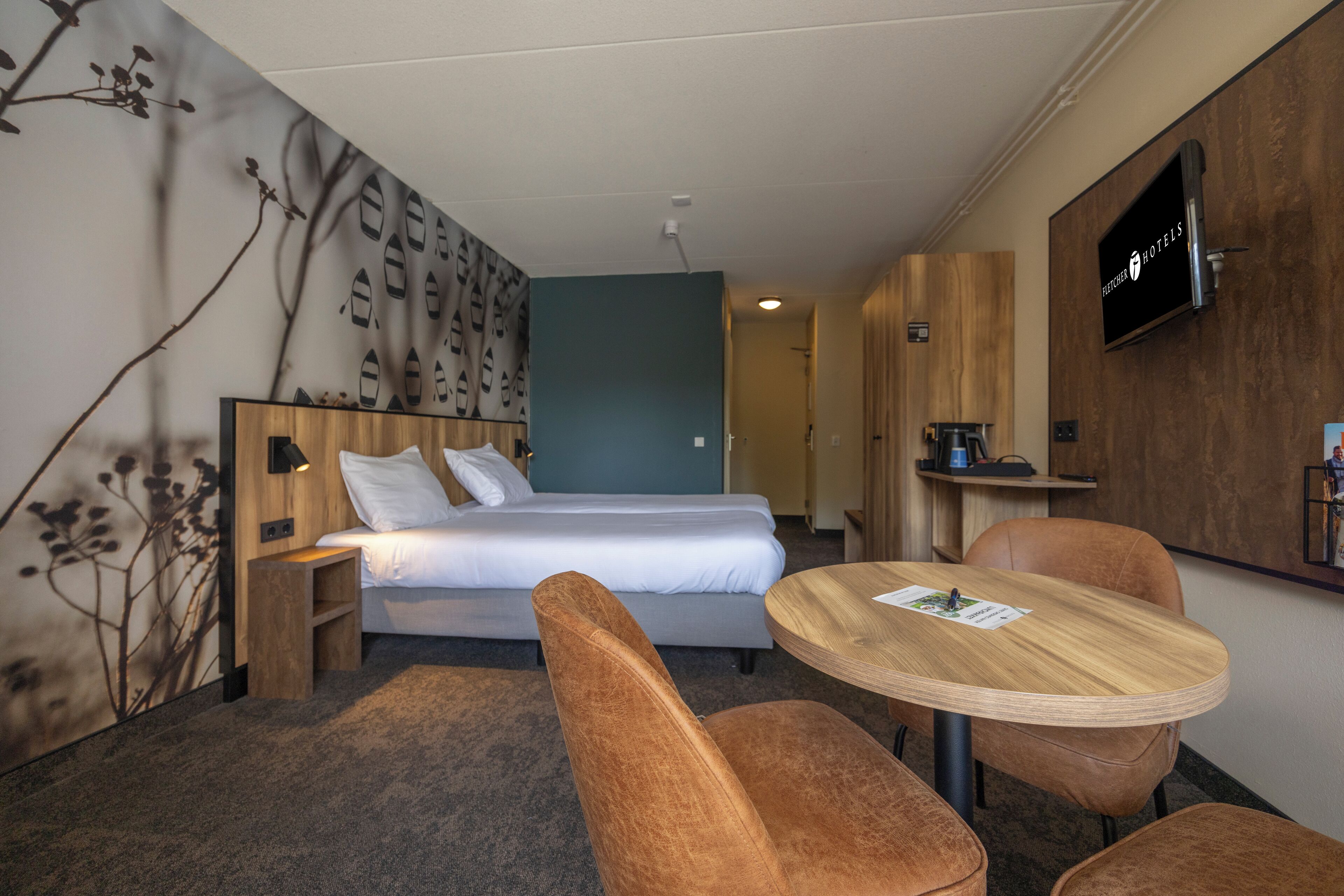A hotel room with a bed, a desk, two chairs, a TV, and a wall with a pattern.