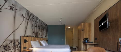 A hotel room with a bed, a desk, two chairs, a TV, and a wall with a pattern.