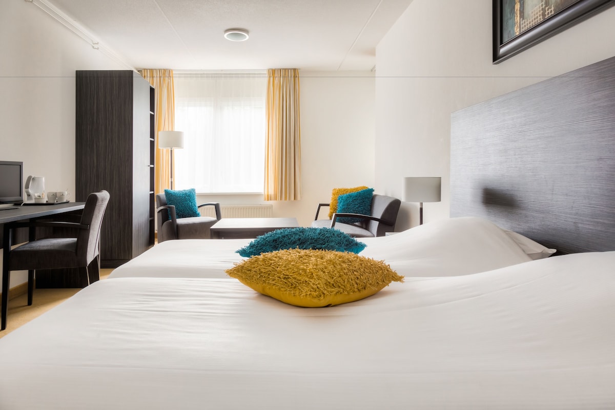 A hotel room with a bed, two chairs, a desk, and a window with curtains.