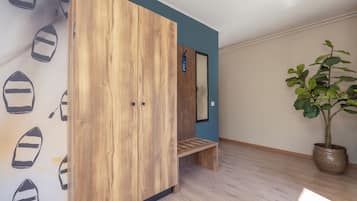 A room with a wooden wardrobe, a bench, a potted plant, and a wall with a boat pattern.