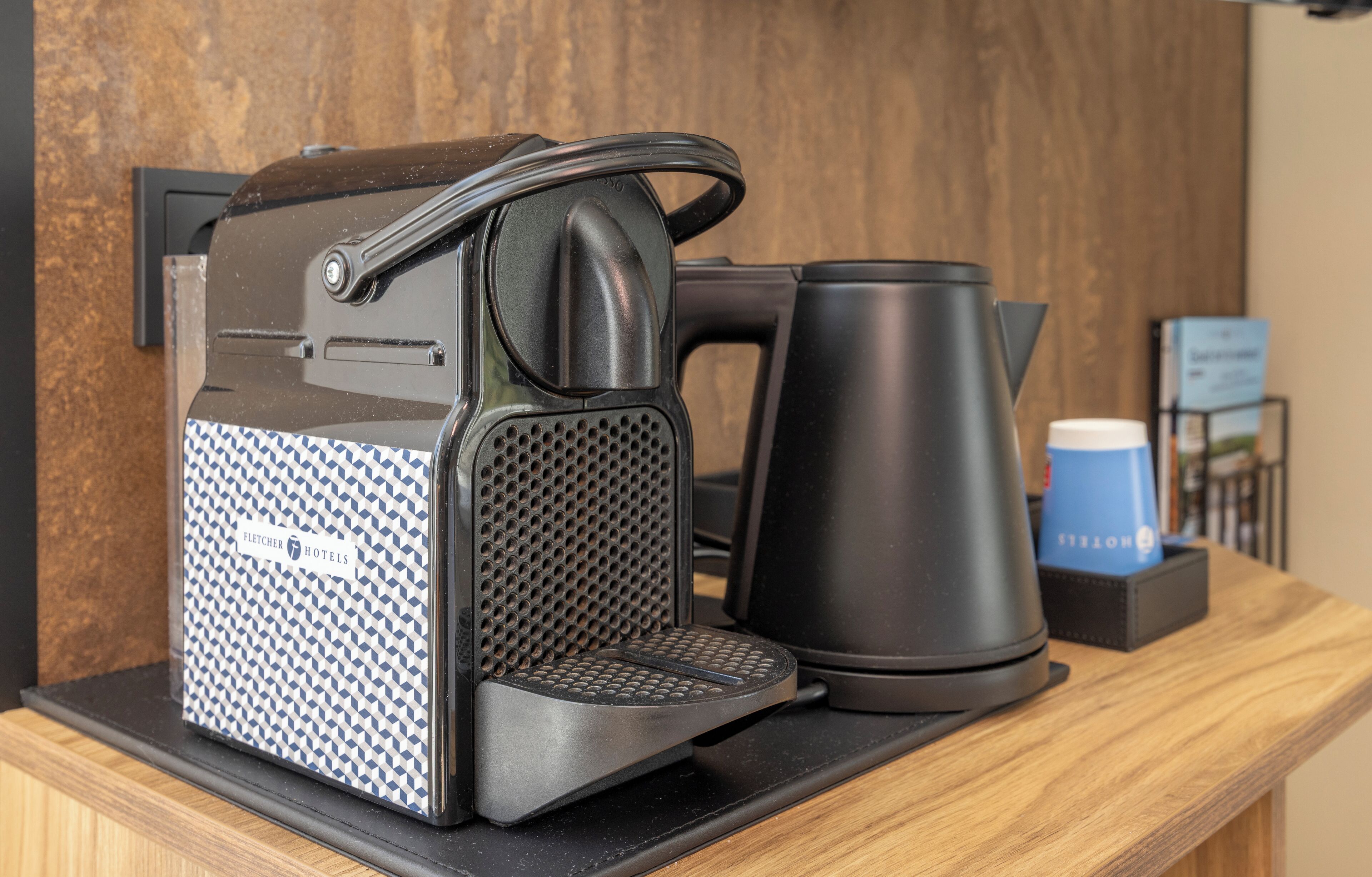 A coffee machine with a handle, a kettle, and a coffee cup on a wooden counter.