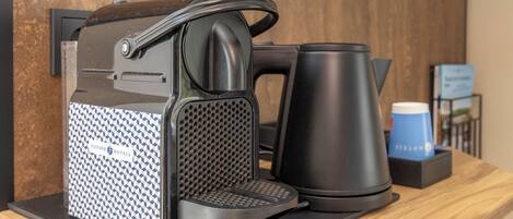 A coffee machine with a handle, a kettle, and a coffee cup on a wooden counter.
