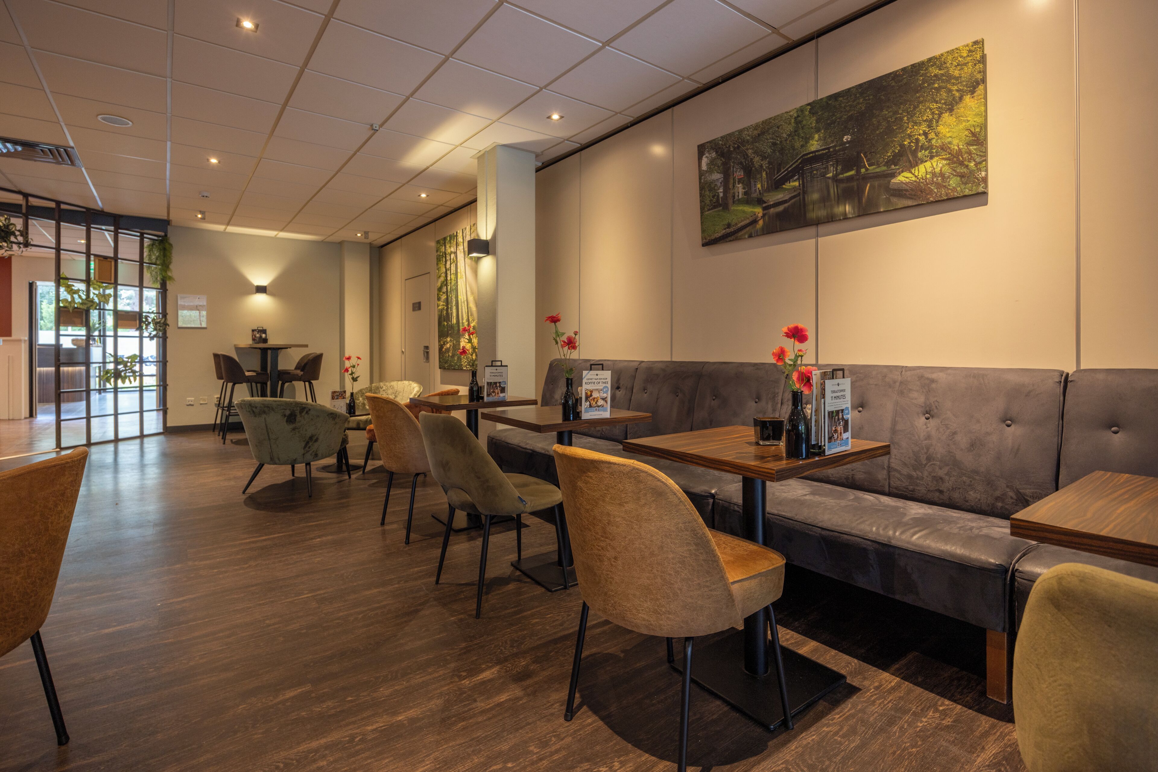 A modern restaurant with wooden tables and chairs, a sofa, and a large painting on the wall.