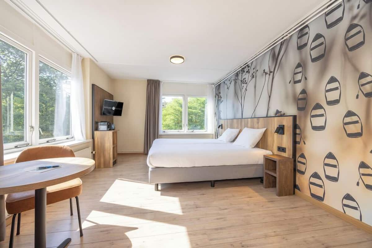 A bedroom with a bed, a desk, a chair, and a TV.