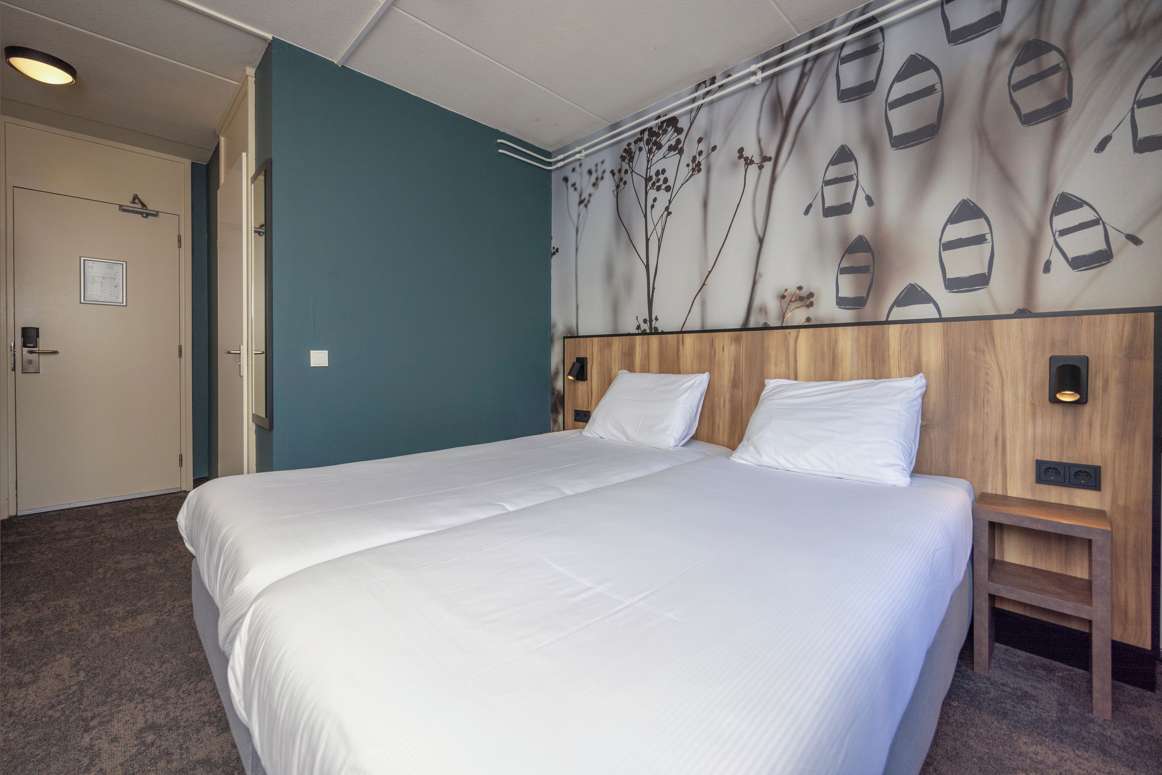 Una cama doble con ropa blanca, un cabecero de madera y una pared con diseño náutico.
