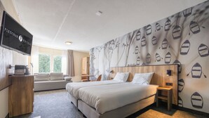 Quarto de hotel com uma cama grande, televisão, cómoda de madeira e parede com padrões náuticos.