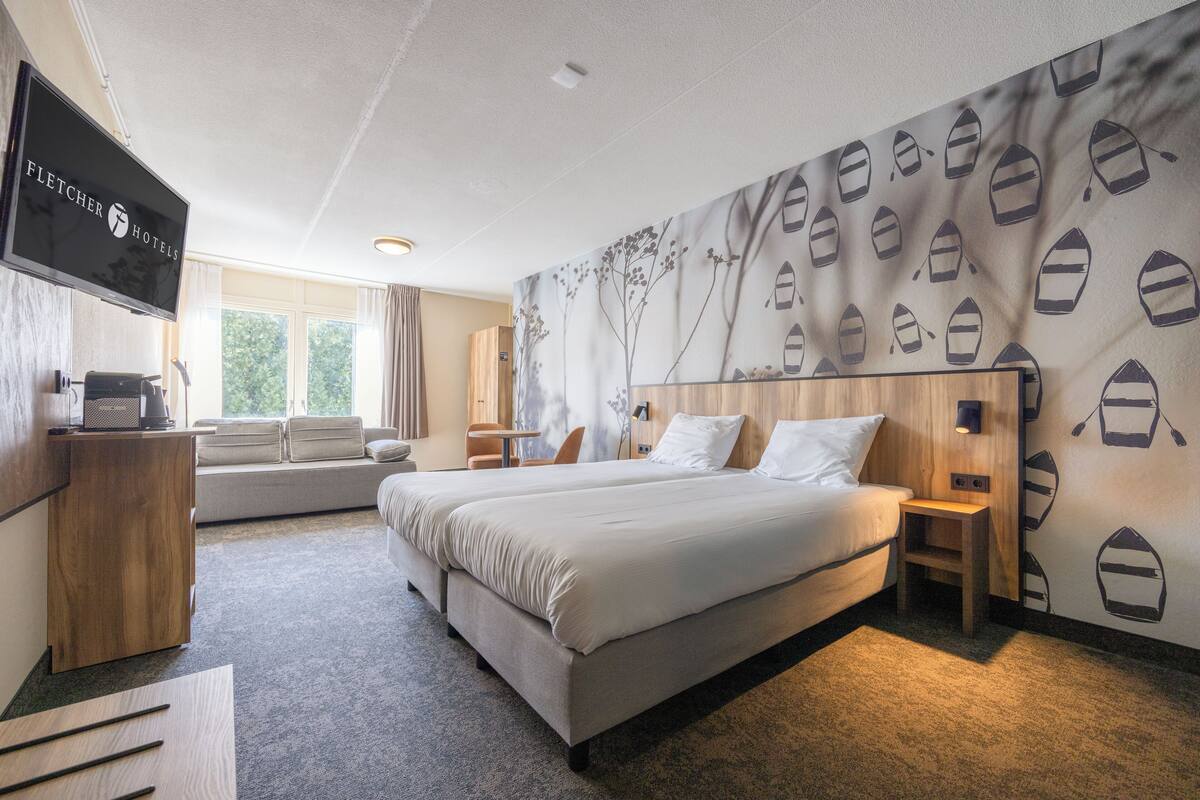 A hotel room with a large bed, a TV, a wooden dresser, and a wall with boat patterns.