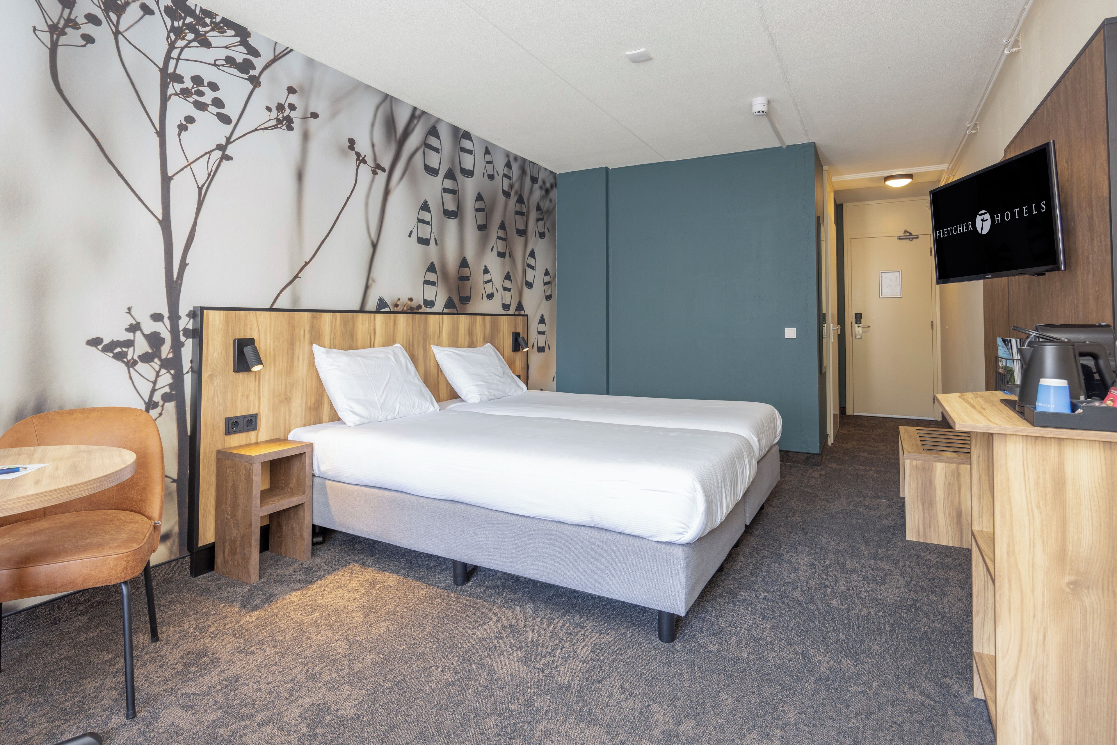A hotel room with a bed, a desk, a chair, and a TV.