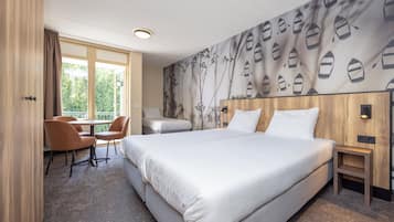 A hotel room with a large bed, a desk with a chair, a window with curtains, and a wall with a boat pattern.