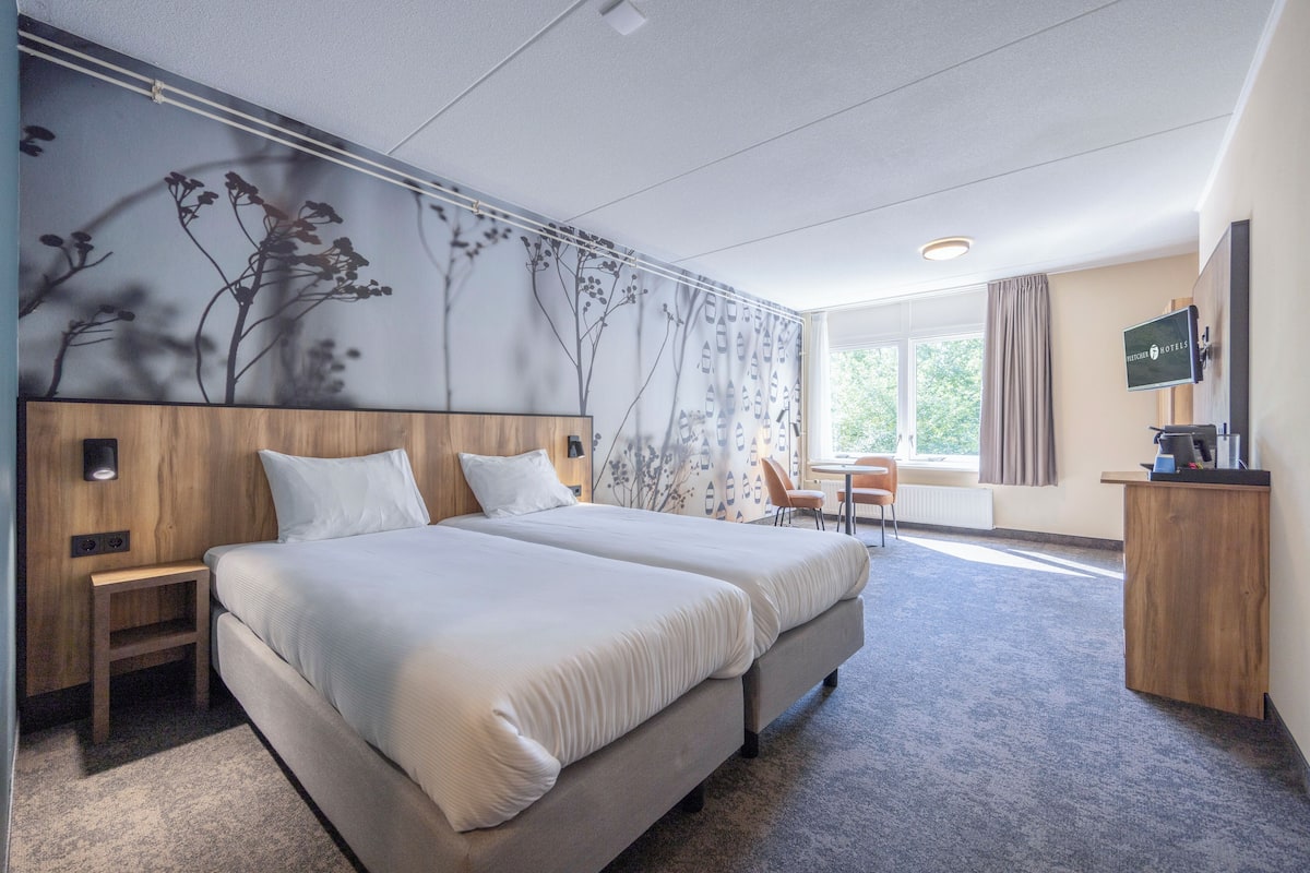 A hotel room with two beds, a desk, a chair, a TV, and a window with curtains.