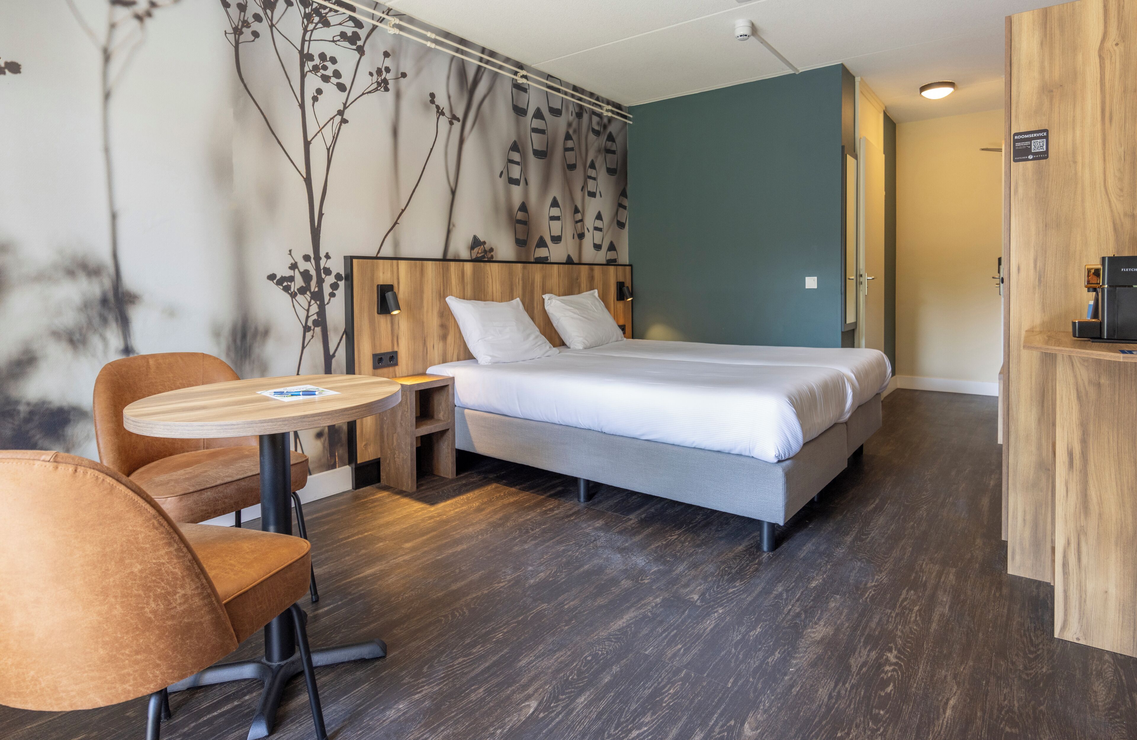 A modern hotel room with a bed, a round wooden table, and a chair.