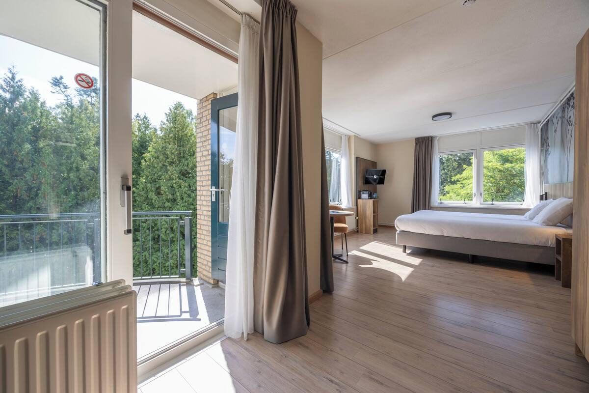A modern hotel room with a balcony, a bed, a desk, and a TV.