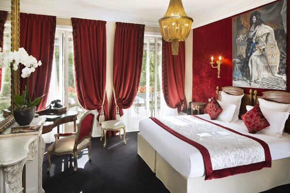 Ein luxuriöses Hotelzimmer mit einem großen Bett, roten Vorhängen, einer Chandelierleuchtre und einem Gemälde an der Wand.