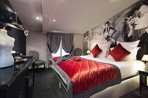 Ein Hotelzimmer mit einem großen Bett, einem Schreibtisch mit Stuhl, einem wandmontierten Fernseher und einem großen Wandgemälde.