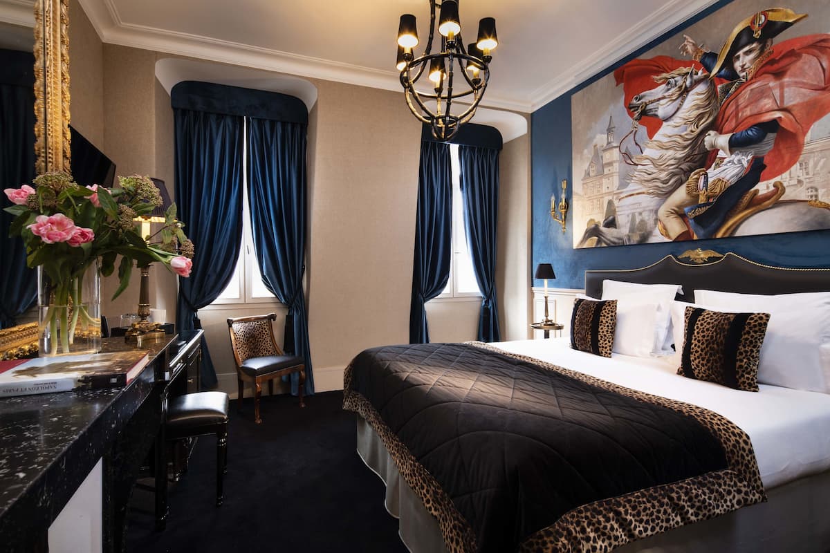 Una habitación de hotel con una cama grande, un escritorio con una silla, un florero y un cuadro en la pared.