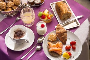 Ein Frühstückstisch mit verschiedenen Speisen, darunter Gebäck, Obst und einem Brot.