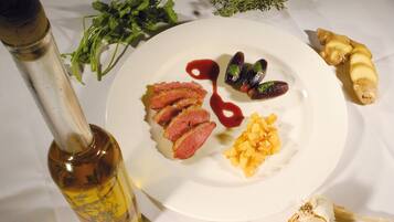 A white table with a bottle of olive oil, a plate with sliced meat, vegetables, and a small dish with spices.