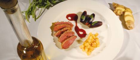 A white table with a bottle of olive oil, a plate with sliced meat, vegetables, and a small dish with spices.