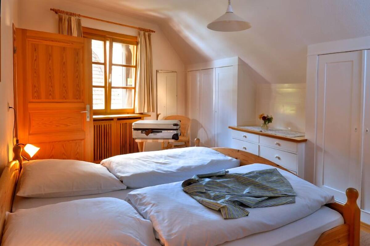 A bedroom with two beds, a wooden wardrobe, a desk with a lamp, and a window with curtains.