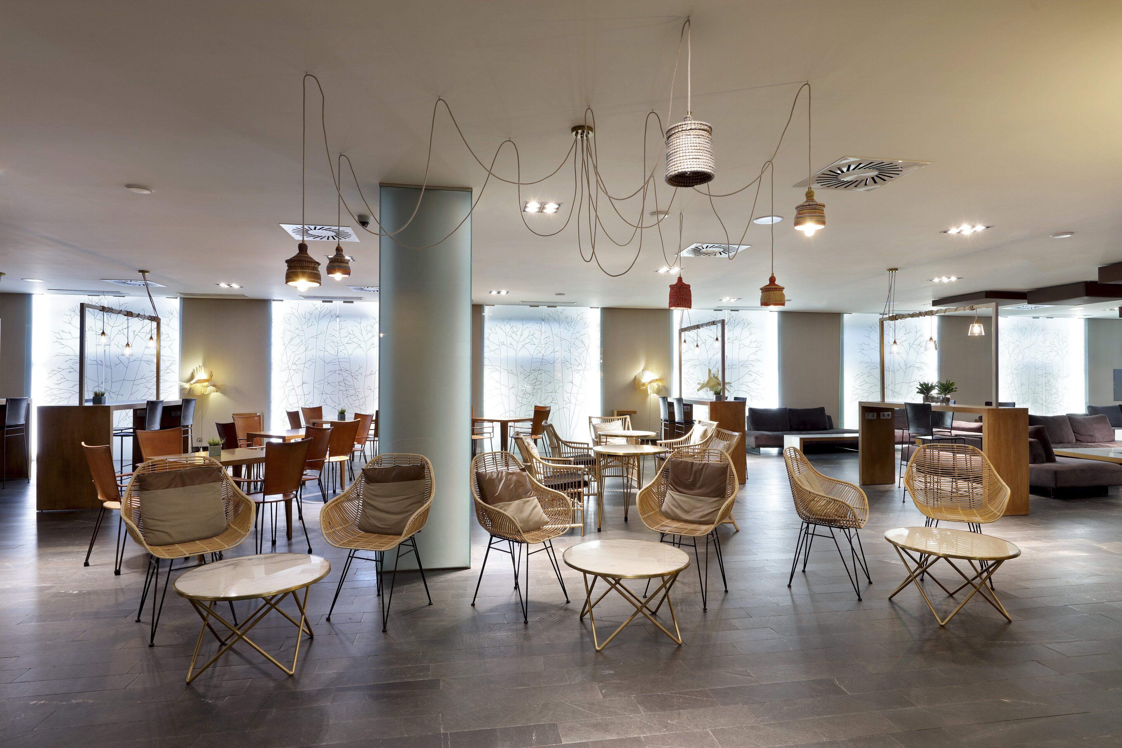 Amplia sala de estar moderna con sillones y mesitas de mimbre, ventanas grandes y lámparas contemporáneas.
