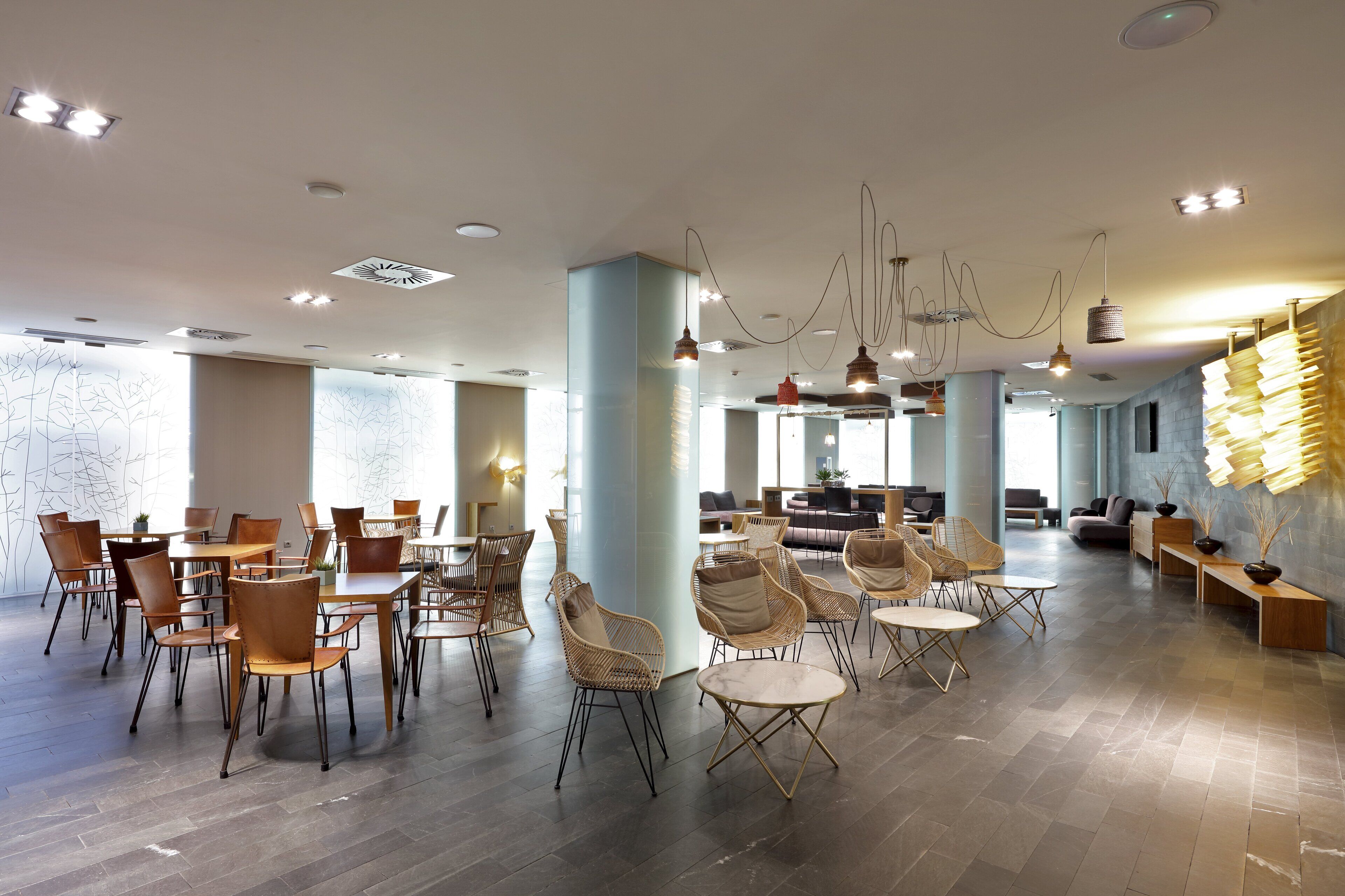 Ett rymligt inomhusområde med flera olika sittgrupper, inklusive bord och stolar, samt en modern takdesign med hängande lampor.