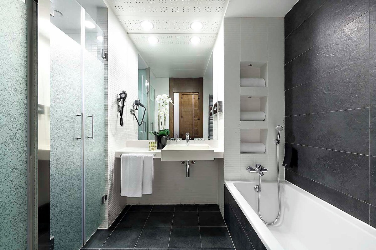 Un baño moderno con cabina de ducha de vidrio, un lavamanos blanco y una pared con azulejos oscuros.