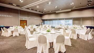 Un salón de conferencias amplio con varias mesas redondas, cada una con mantel blanco, sillas y cubertería.
