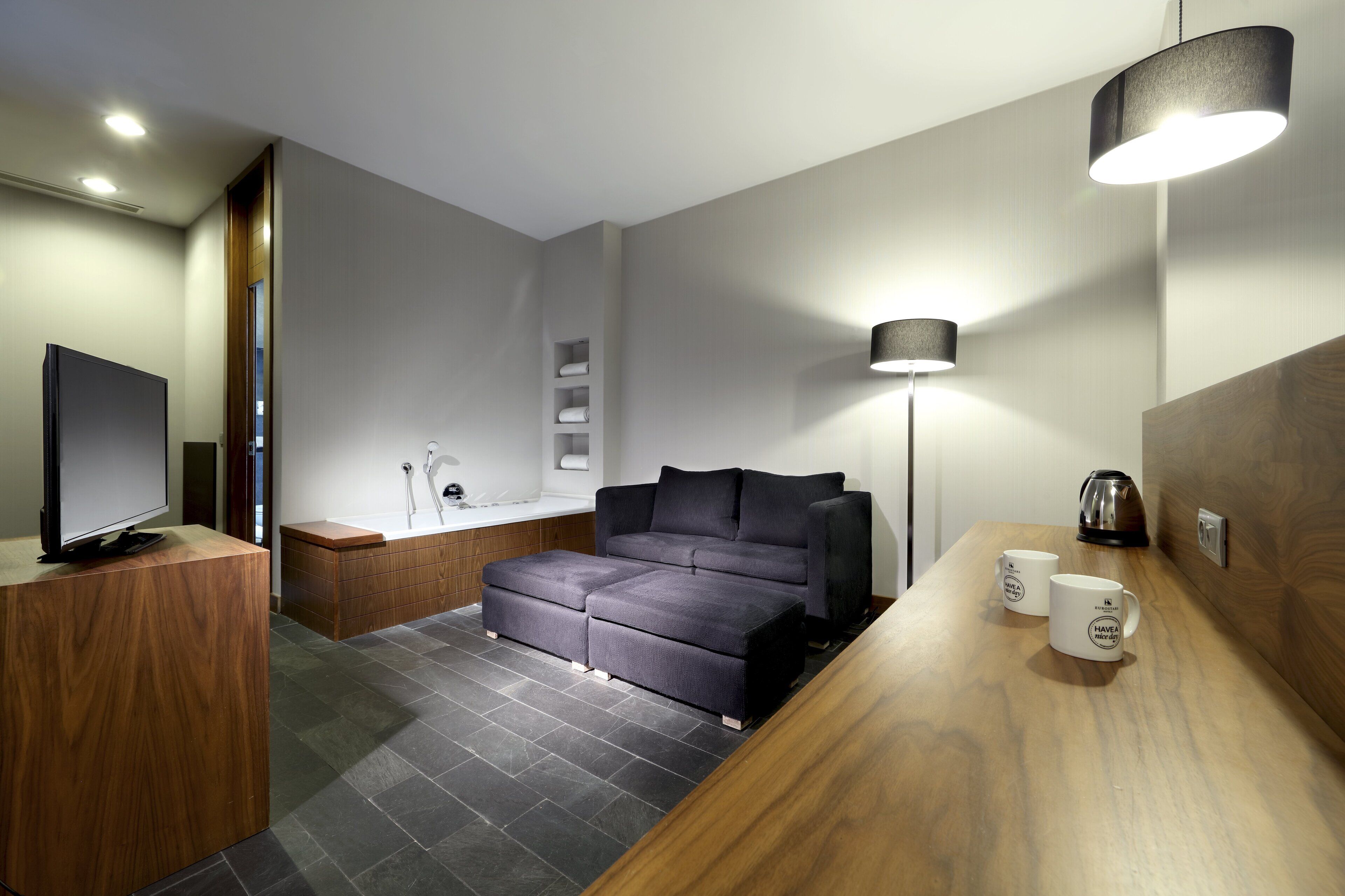 Una habitación de hotel moderna con sofá, televisión, cafetera y lámpara.