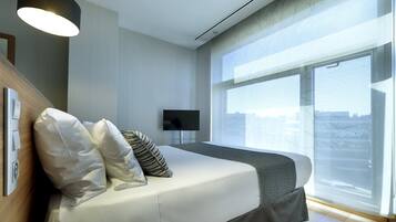 Una habitación de hotel moderna con una cama grande, un televisor de pantalla plana y un ventanal con vistas a la ciudad.