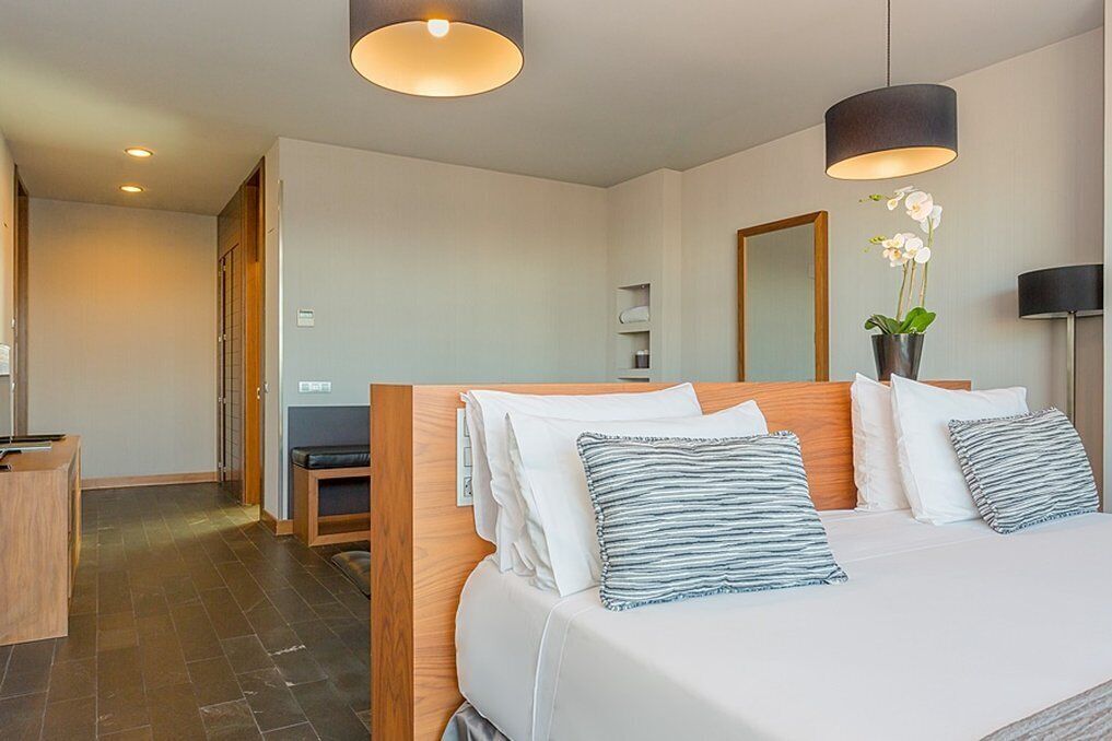 A modern hotel room with a large bed, wooden headboard, and two pendant lights.