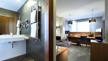 A modern bathroom with a large sink, towel rack, and a wooden vanity. The room features dark tiles, a wooden door, and recessed lighting.