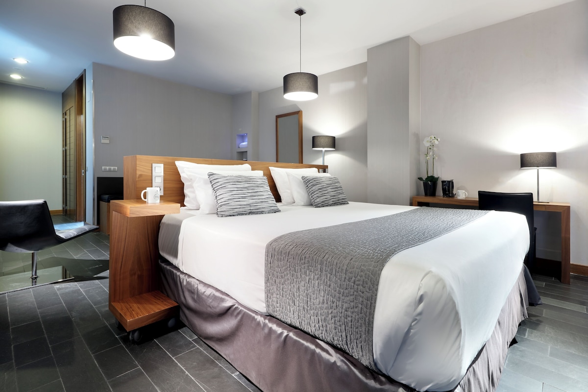 Una habitació d'hotel moderna amb un llit gran, taules de nit, un escriptori i una cadira.
