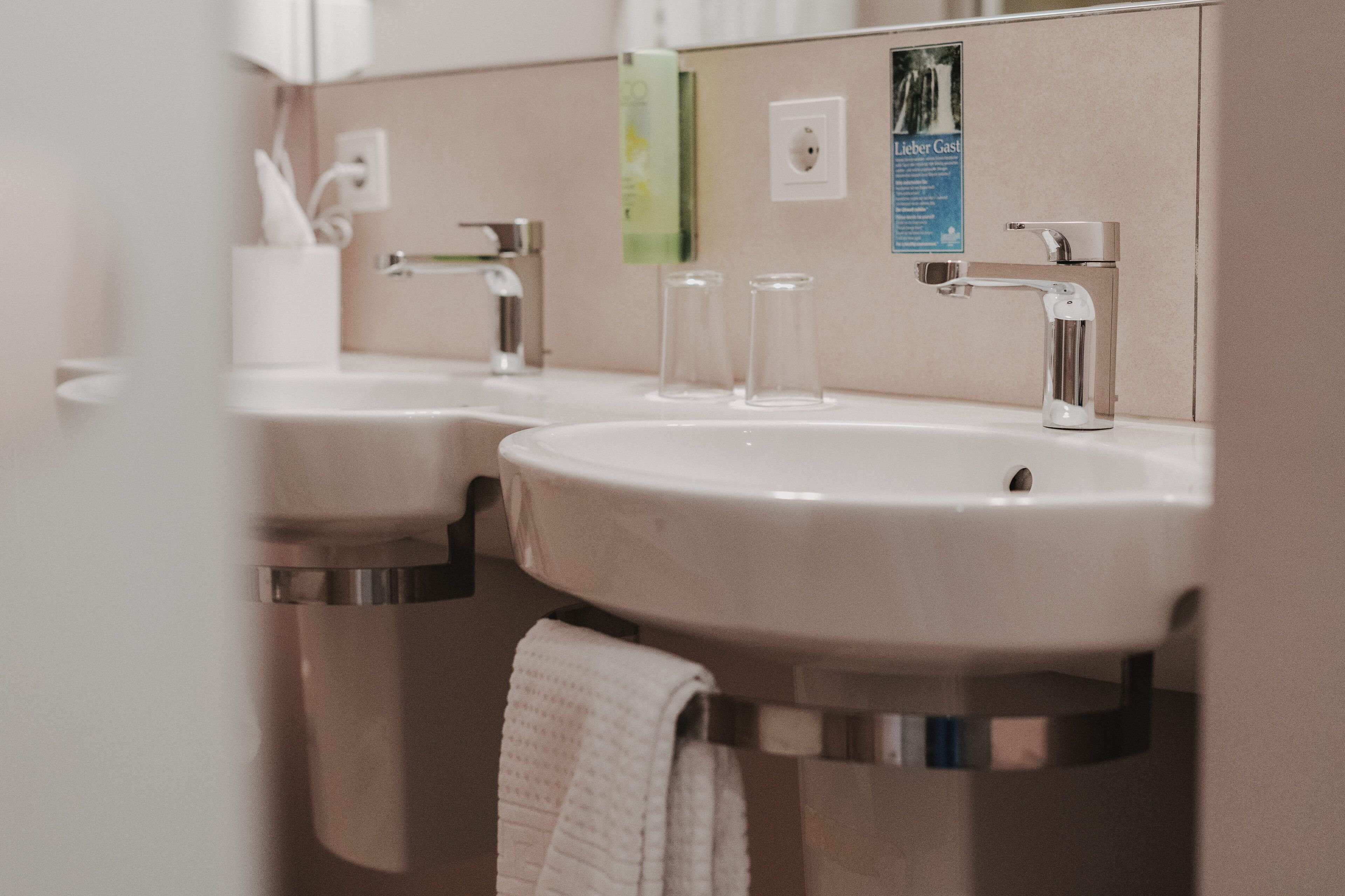 A bathroom with two sinks, a towel hanging, and a mirror.