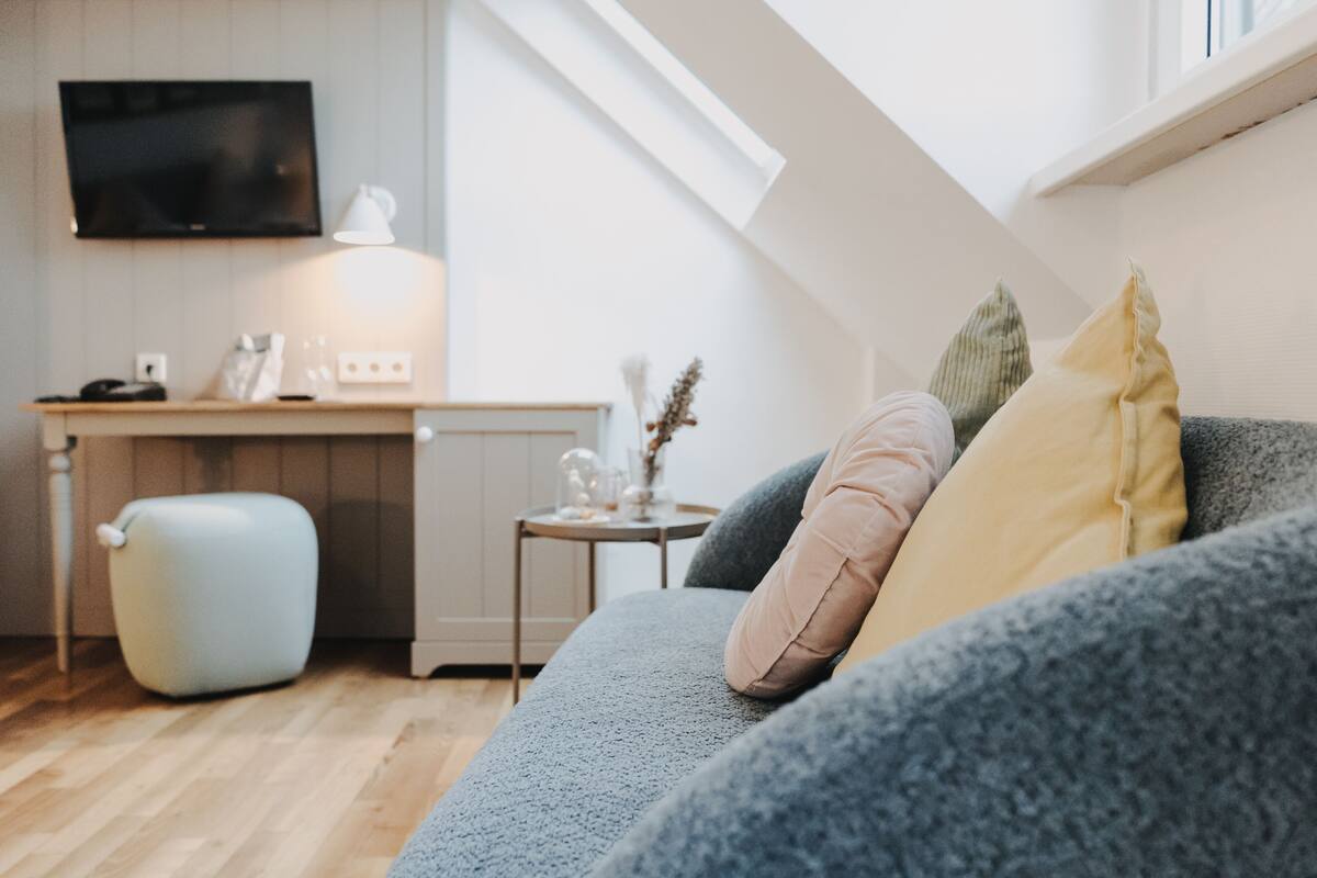 A cozy living room with a grey sofa, a small side table, and a television mounted on the wall.