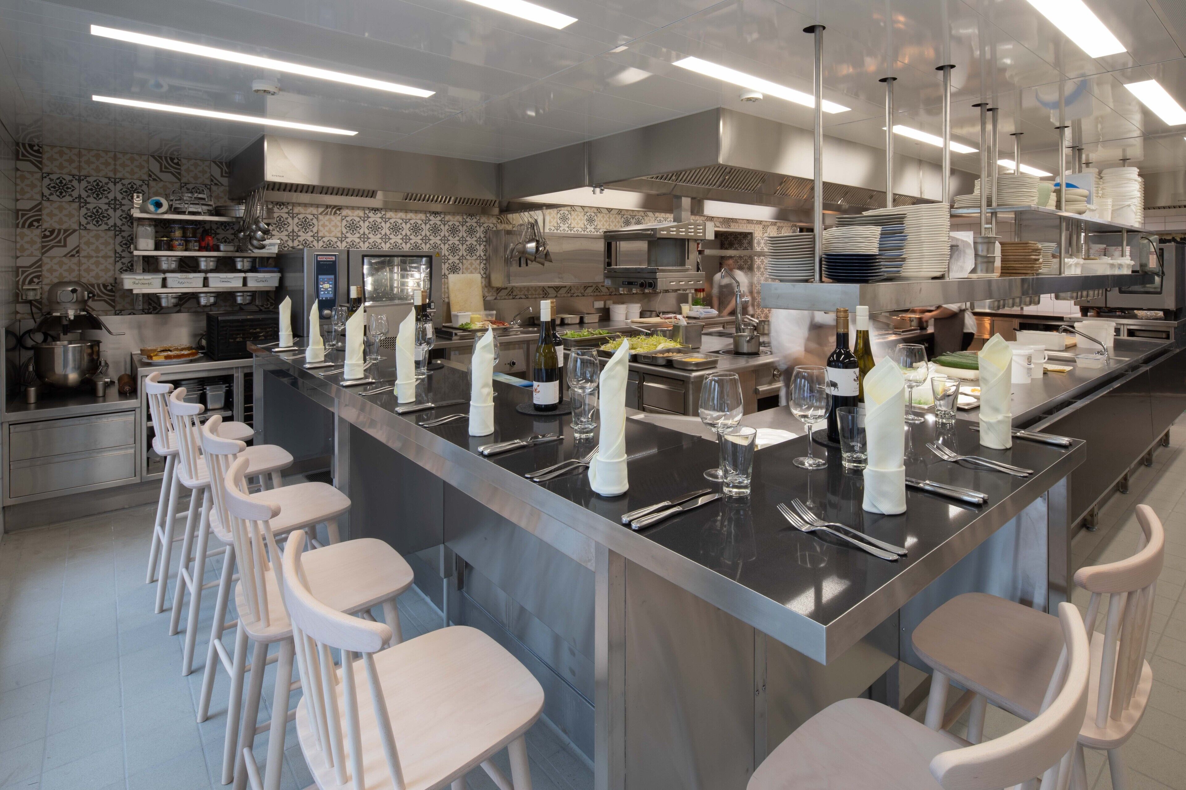 A modern kitchen with stainless steel appliances, a long bar area with stools, and neatly arranged dishes and glasses.