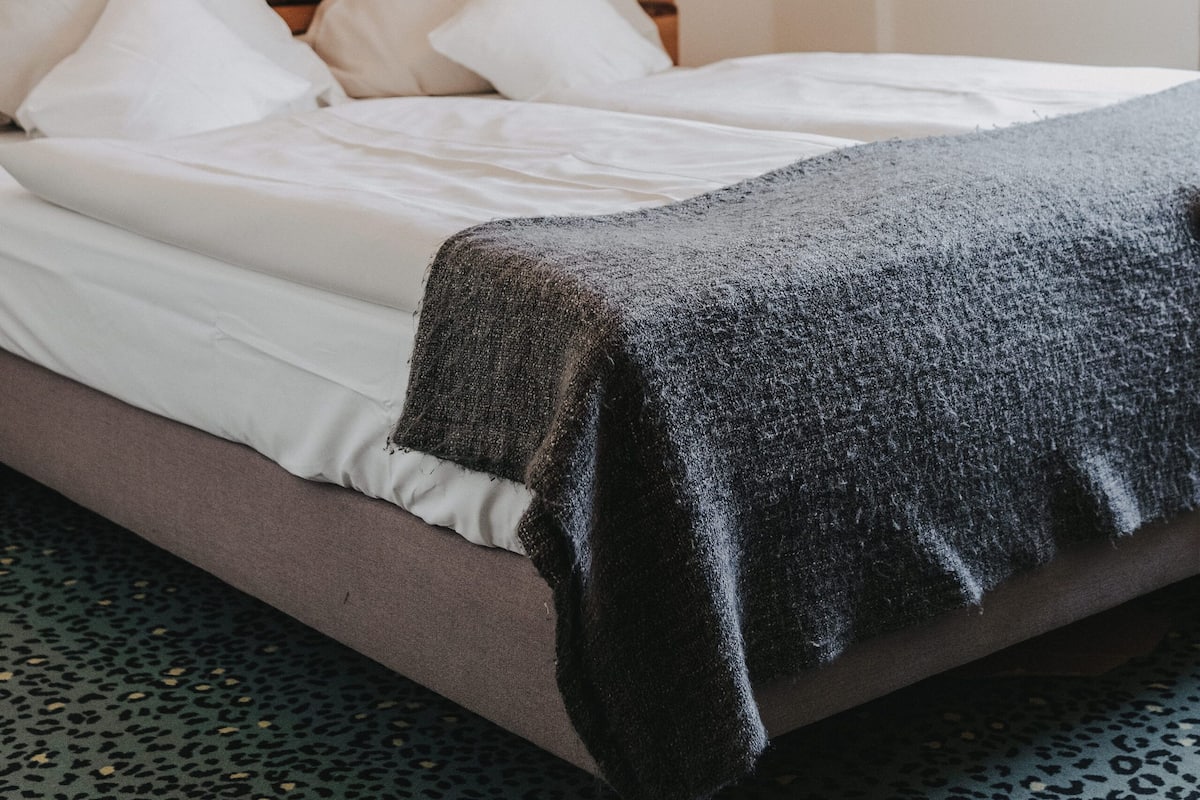 A bed with white linens, a dark blanket, and three white pillows.