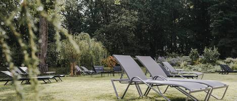Une rangée de chaises longues sur une pelouse, dans un espace extérieur, avec des arbres en arrière-plan.