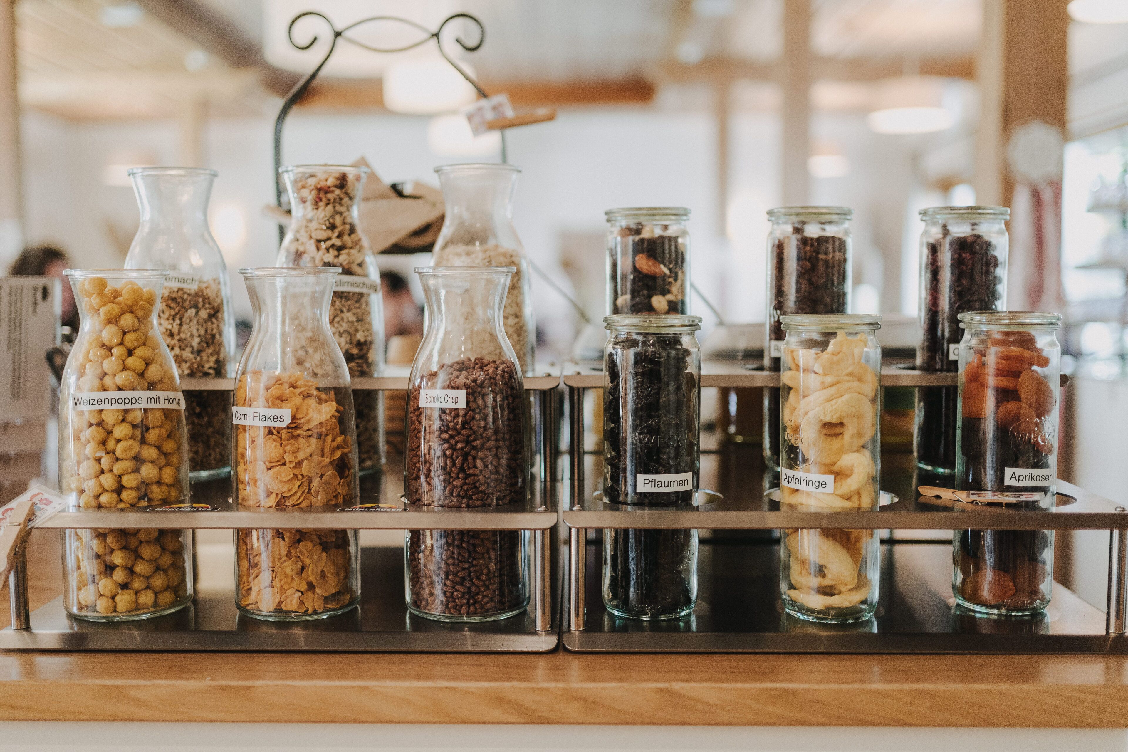 A display of various grains and seeds in glass jars, each labeled with their name.