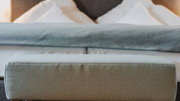 A neatly arranged bed with pillows, a bedside table, and a bench. There are framed pictures on the wall above the bed.