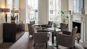 A room with a round table, four chairs, a fireplace, and a view of buildings through large windows. - Montagu Place Hotel (London)