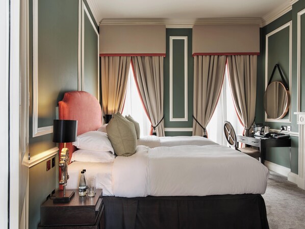 Una habitación de hotel ordenada con una cama grande, una mesita de noche con lámpara, un aparador y un espejo.