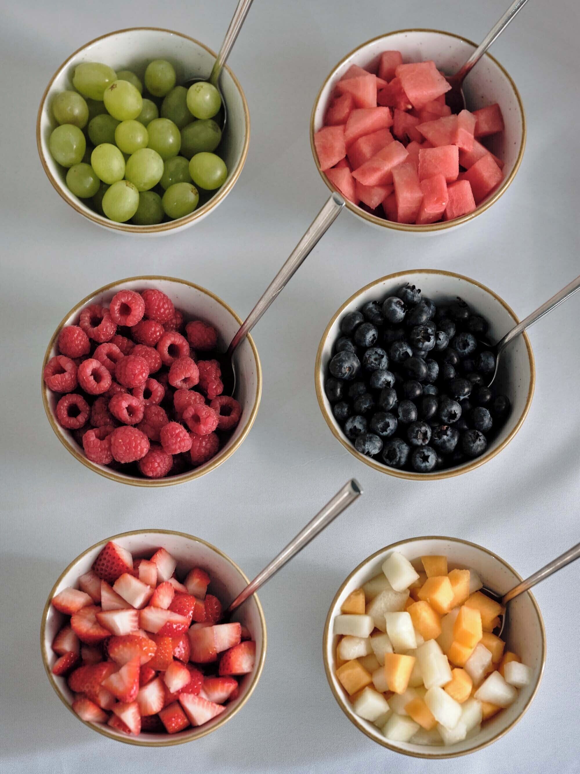 Six bowls of various fruits on a table.