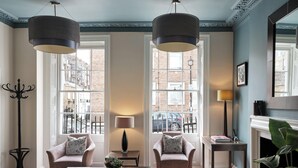 A spacious living room with a large window, a fireplace, and a modern chandelier. - Montagu Place Hotel (London)