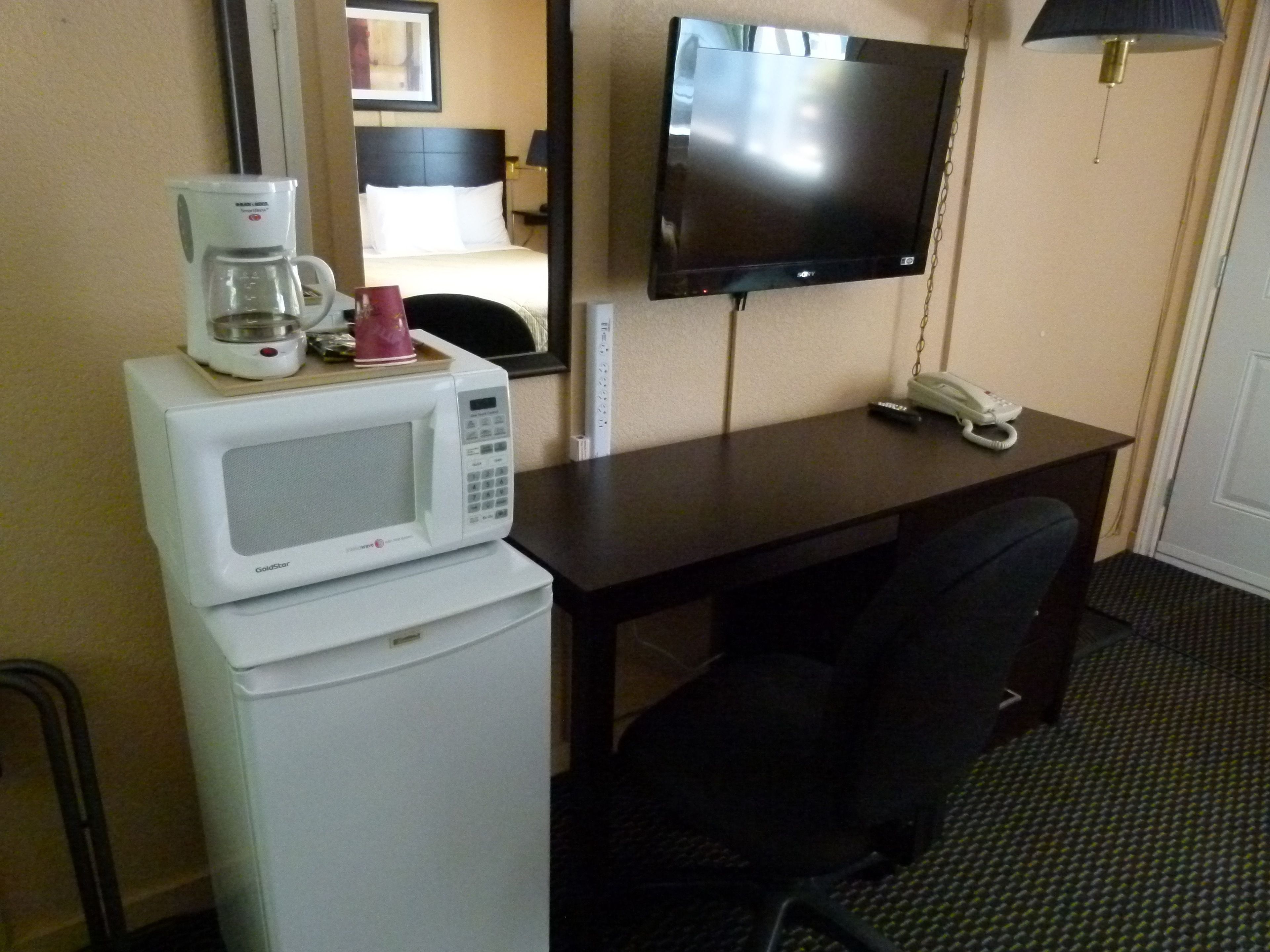 Una habitación de hotel con escritorio, televisor montado en la pared, microondas y cafetera.