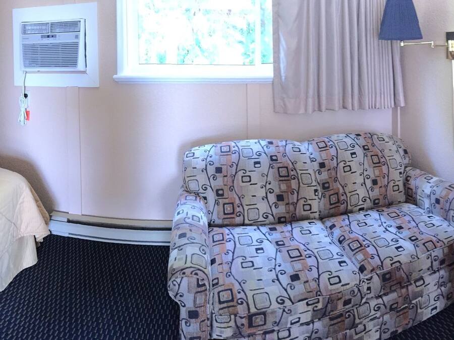 Habitación de hotel con una cama, un sillón estampado, una mesita redonda pequeña, un microondas y un televisor.
