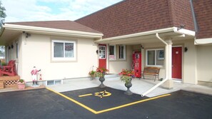 A building with a red door, a bench, and a parking space marked with a wheelchair symbol. - Country Squire Motel (Arnprior)