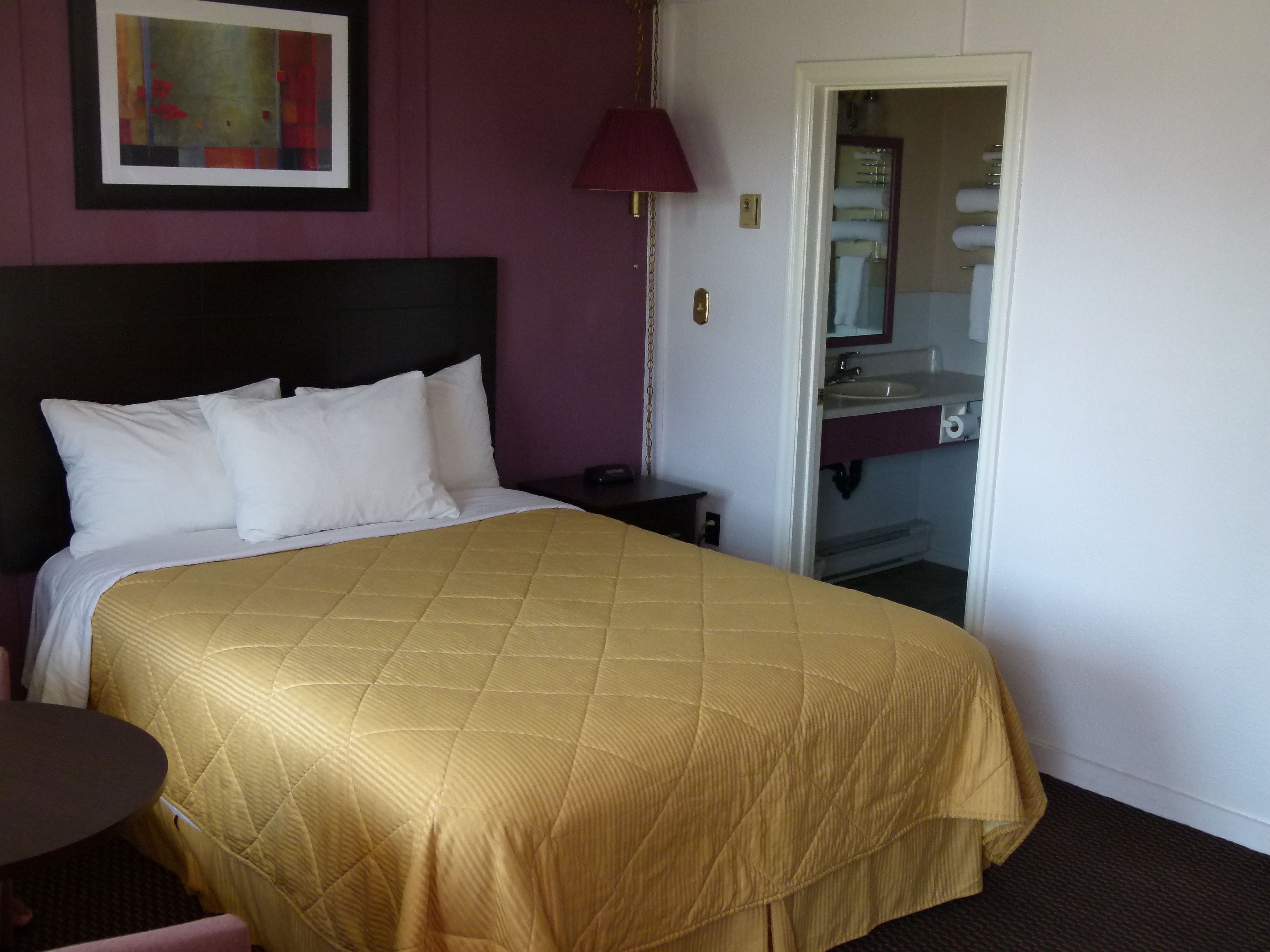 A hotel room with a bed, a nightstand, a lamp, and a bathroom visible through an open door.