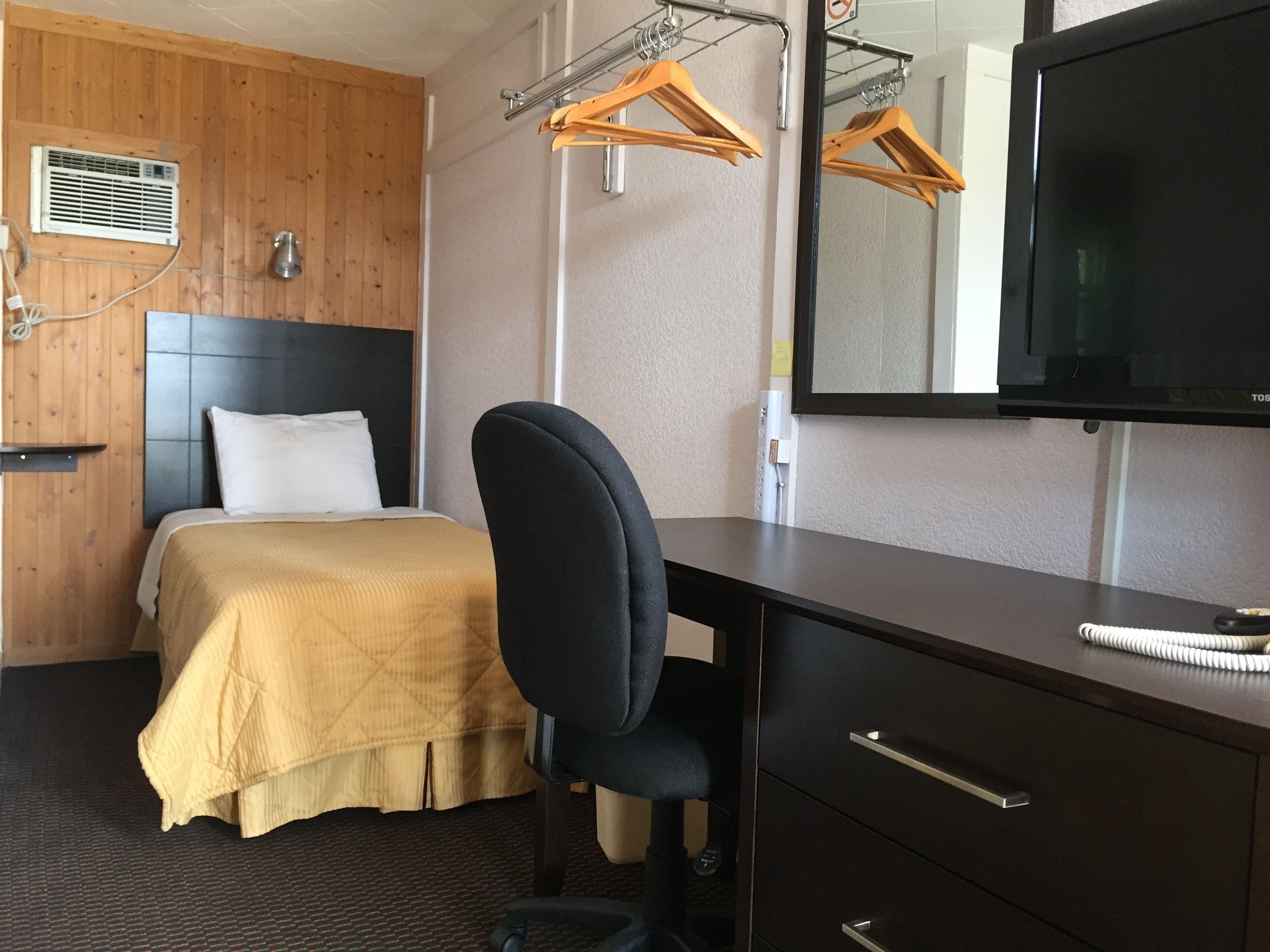 A hotel room with a bed, a desk, a chair, a TV, and a coat rack with hangers.