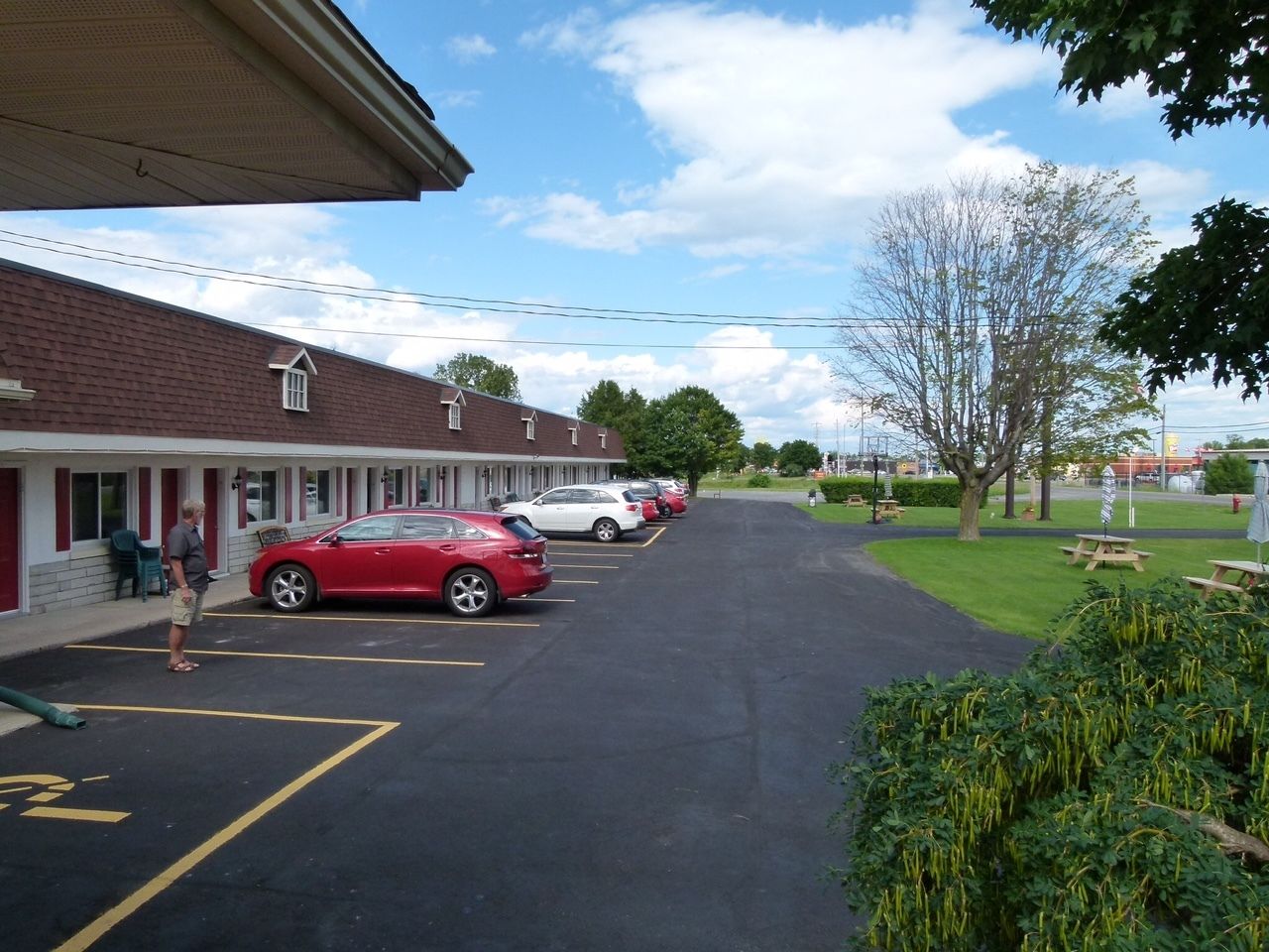 A motel with a parking lot, a red car, and a white car parked.